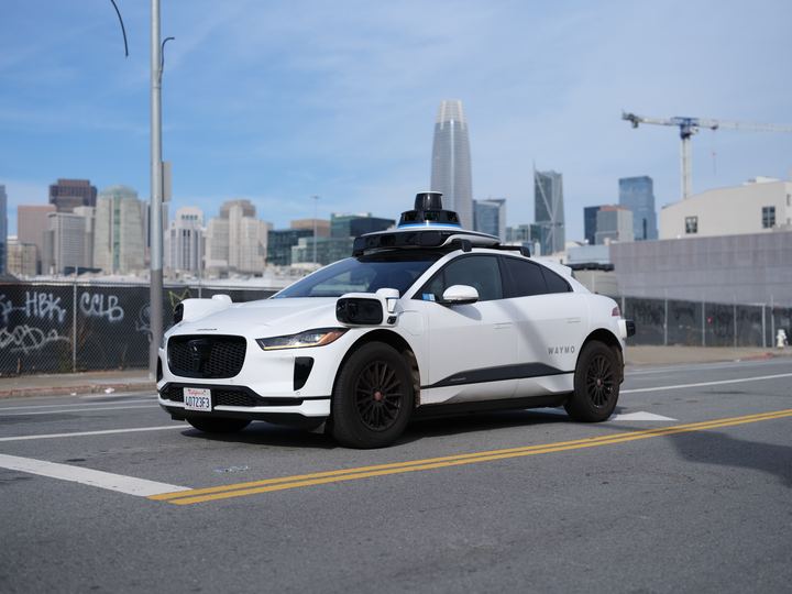 A white self-driving electric SUV with roof sensors on a San Francisco street