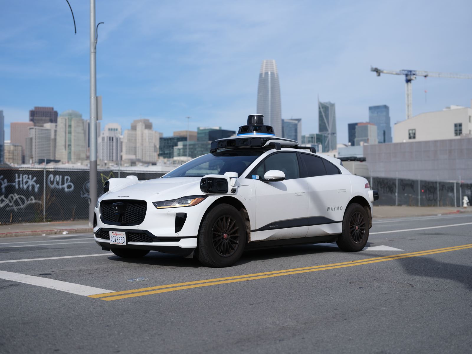 A white self-driving electric SUV with roof sensors on a San Francisco street